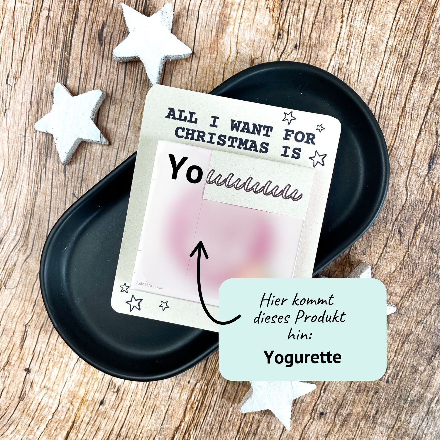 Lustiger Adventskalender mit Yogurette Vorlage – Druckvorlage für Weihnachten Karte mit Aufschrift „All I want for Christmas is You“ und Platz für eine Yogurette-Schokolade. Liegt auf schwarzer Schale mit weißen Holzsternen. Liebevolle Druckvorlage für ein kleines Weihnachtsgeschenk zum Selbermachen.