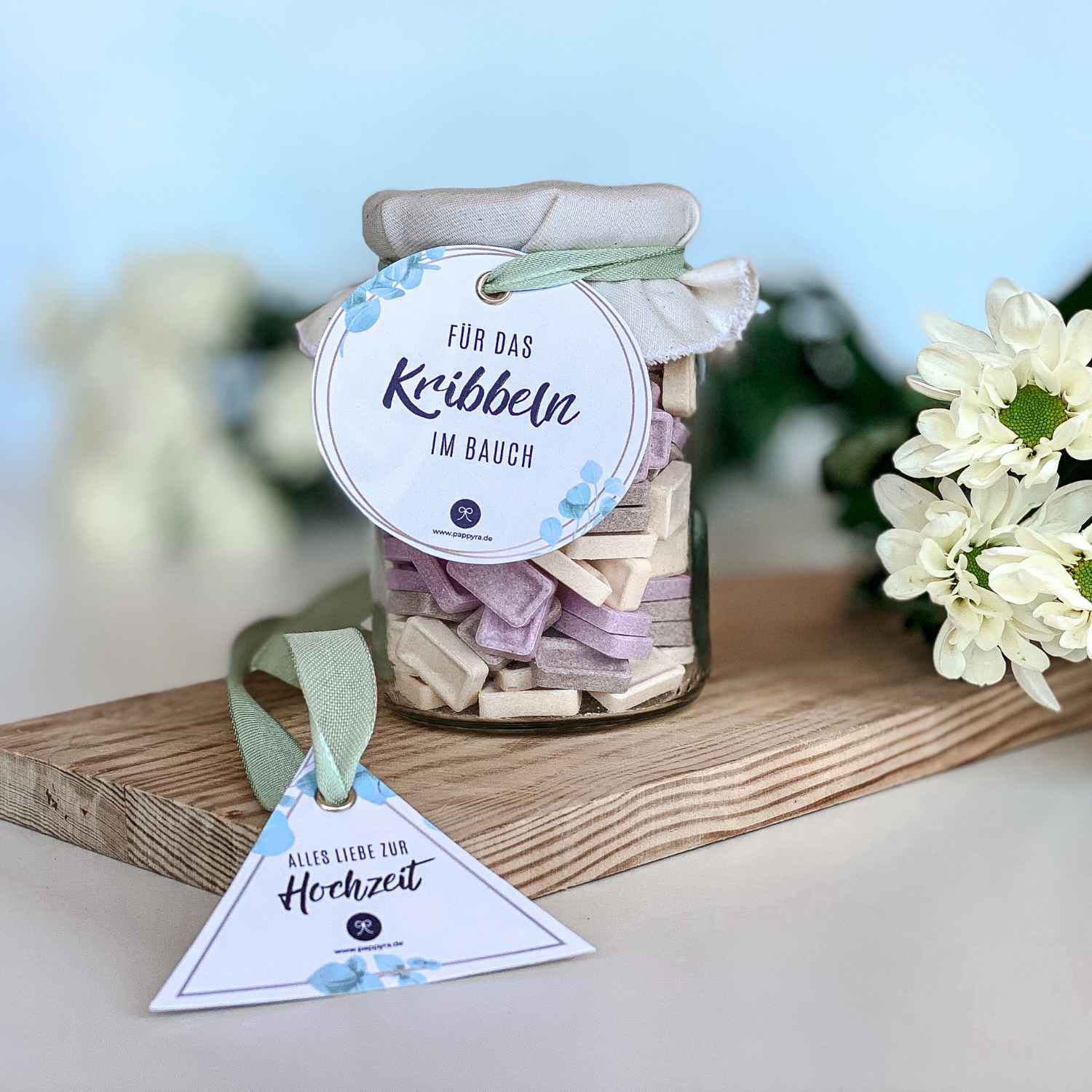 Fertiges Brauseglas Geschenk zur Hochzeit DIY Ein liebevoll verpacktes Glas mit Stoffdeckel und Anhängern auf einem Holzbrett dekoriert mit Blumen als fertiges Beispiel für ein Geschenk zur Hochzeit DIY.