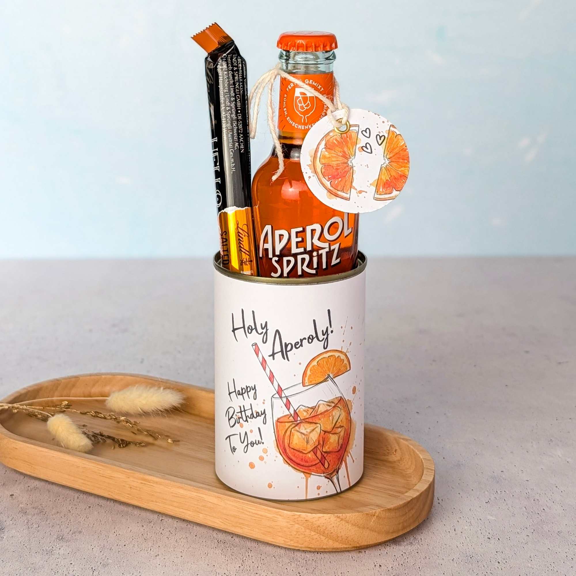 Eine kreative Aperol Geschenkidee zum Geburtstag. Eine upgecycelte Konservendose, verziert mit der digitalen Druckvorlage "Holy Aperoly", ist befüllt mit einer kleinen Flasche Aperol Spritz und Schokolade – ideal als schnelles DIY Geschenk und Last Minute Geschenk.