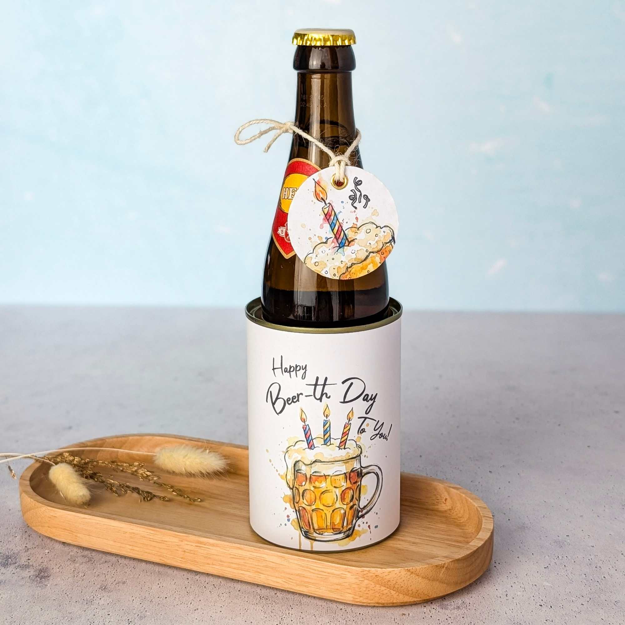 Bier Geschenk Bierflasche lustiges Etikett Eine braune Bierflasche wird als originelles Bier Geschenk auf einem kleinen Holztablett neben getrockneten Blumen präsentiert. Die Flasche steckt in einer Banderole mit der Aufschrift 'Happy Beer-th Day To You!' und dem Aquarell-Motiv eines Bierkrugs mit Geburtstagskerzen. Am Flaschenhals ist ein passendes, lustiges Etikett an einer Kordel befestigt. Eine perfekte Idee für ein persönliches DIY Geschenk: Einfach die digitale Druckvorlage als PDF Vorlage herunterladen, ausdrucken und im Handumdrehen ein kreatives Last Minute Geschenk basteln.